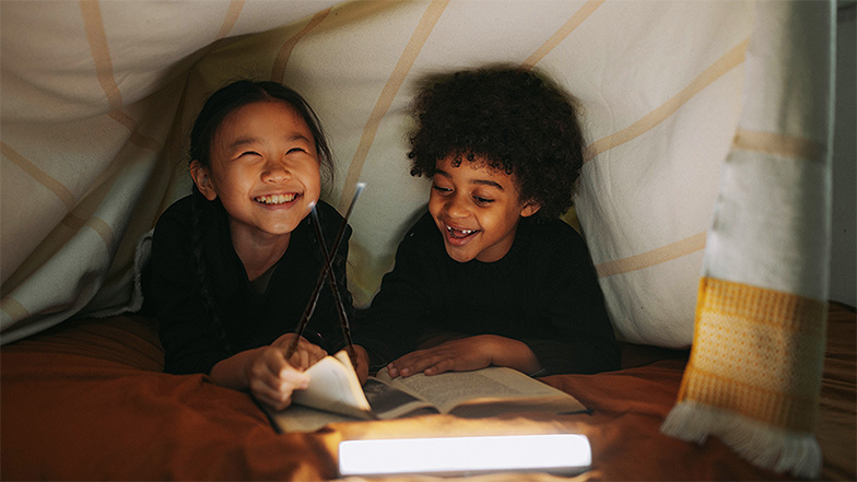 Children reading a book under covers